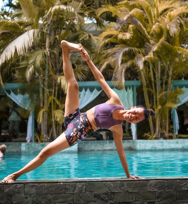 Woman smiling serenely while performing a yoga stretch outdoors.